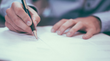 Hand holding a pen to a sheet of paper while the other hand hold the paper in place