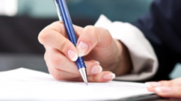 Hand holding a pen which is pressed to a sheet of paper